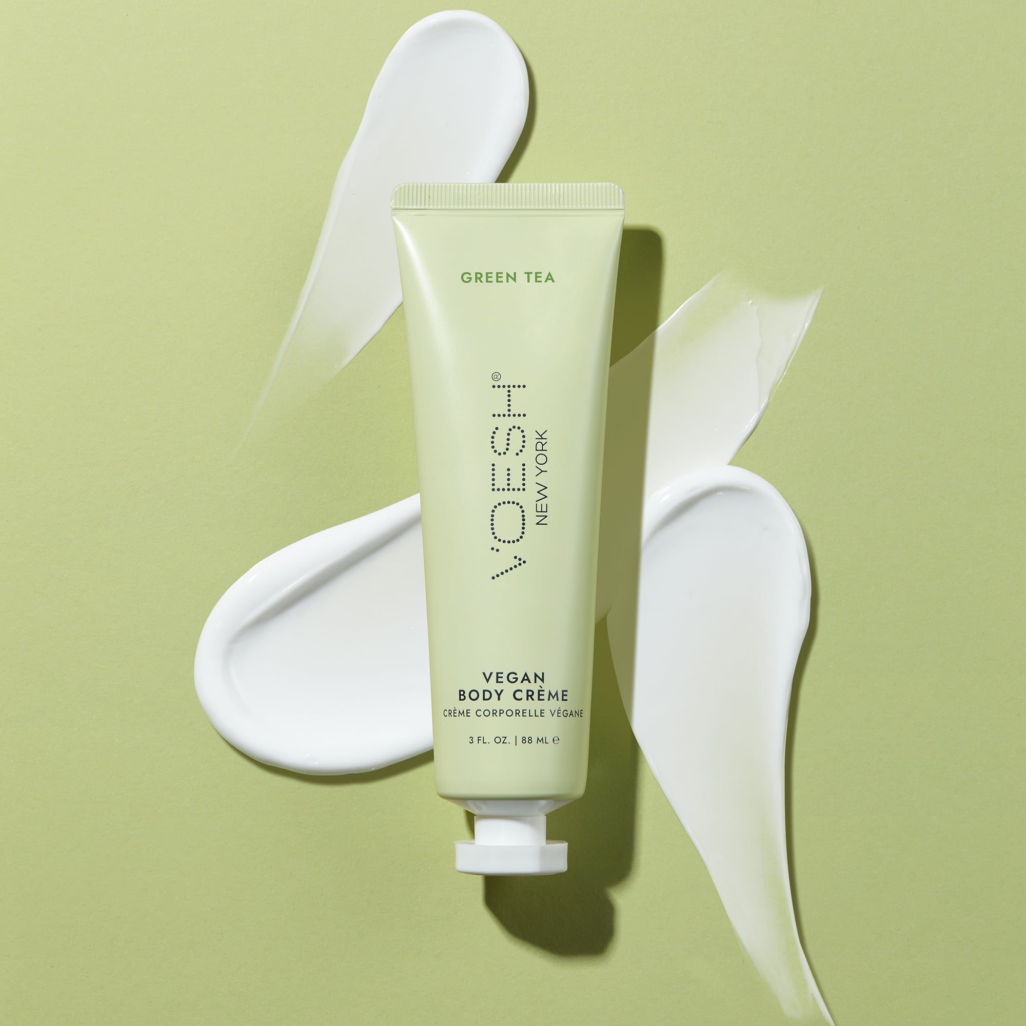 Vegan Body Crème Green Tea pictured on top of the lotion’s texture on a green background.